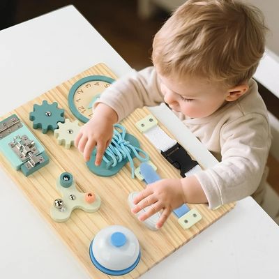 Bébé manipulant une planche d’activité Montessori en bois avec lacet, engrenages et boutons, jouet éducatif favorisant la motricité fine et l’éveil sensoriel
