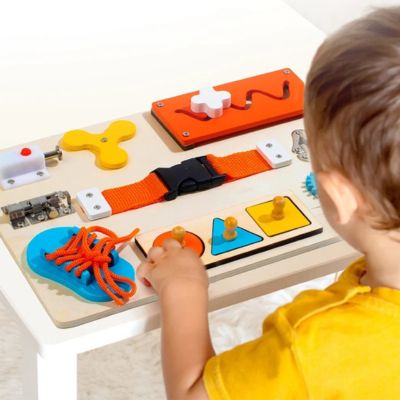 Enfant manipulant une planche d’activité Montessori en bois avec formes, lacet et systèmes à actionner, jouet éducatif développant la motricité fine et la coordination
